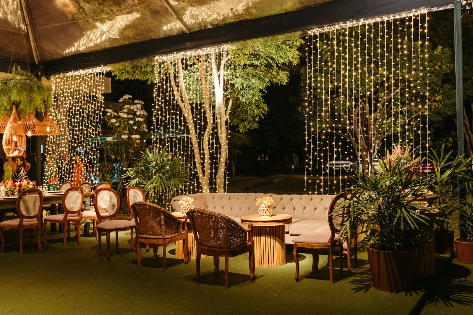 Outdoor lounge at night framed by curtain string lights and woven pendants